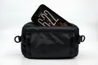 An Alpha Pack from the back showing a phone sticking out of the dedicated phone pocket  | Color: Black VX | Size: 1.8L
