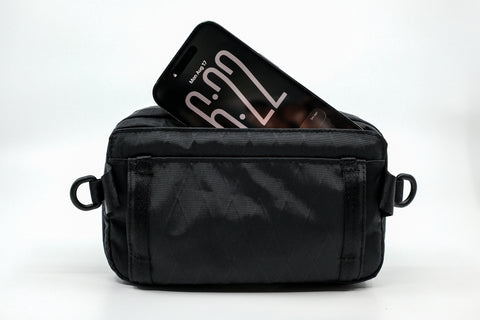 An Alpha Pack from the back showing a phone sticking out of the dedicated phone pocket  | Color: Black VX | Size: 1.8L
