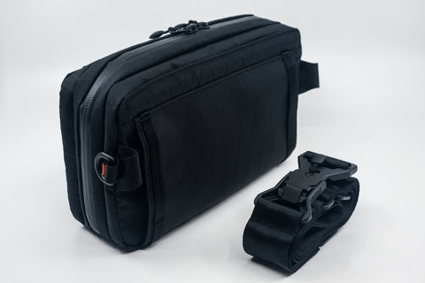 An Alpha Pack shown from the back at a three quarter angle with rolled up strap and Fidlock buckle  | Color: Black VX | Size: 2.6L