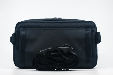 An Alpha Pack shown from the back with rolled up strap and Fidlock buckle | Color: Black VX | Size: 2.6L