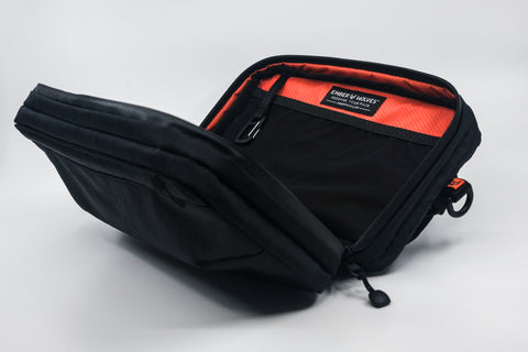 An Alpha Pack shown open from the front at three quarter angle displaying its internal carabiner and label  | Color: Black VX | Size: 2.6L